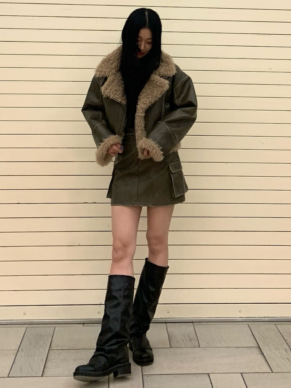 グリーン系のムートンコート、ブラック系のニット/セーター、グリーン系のスカートを着用したレディースの冬コーディネートの2枚目の写真