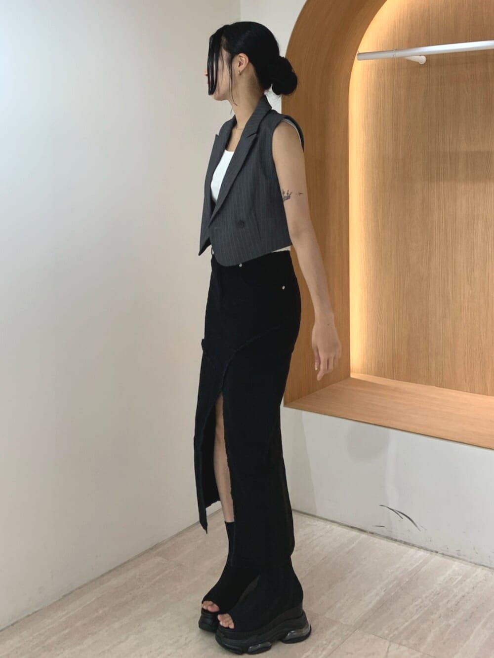 グレー系のベスト、ブラック系のサンダル、ブラック系のデニムスカートを着用したレディースの夏コーディネートの2枚目の写真