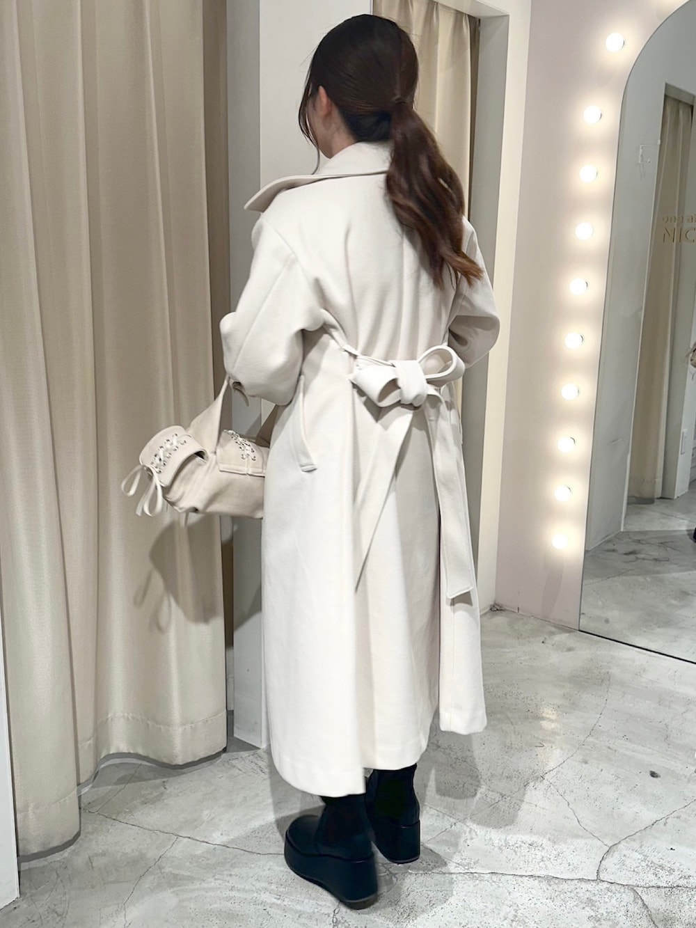 ホワイト系のステンカラーコート、ホワイト系のショルダーバッグ、ブラック系のブーツを着用したレディースの冬コーディネートの4枚目の写真