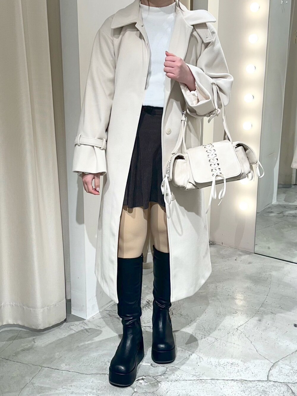 ホワイト系のステンカラーコート、ホワイト系のショルダーバッグ、ブラック系のブーツを着用したレディースの冬コーディネートの2枚目の写真