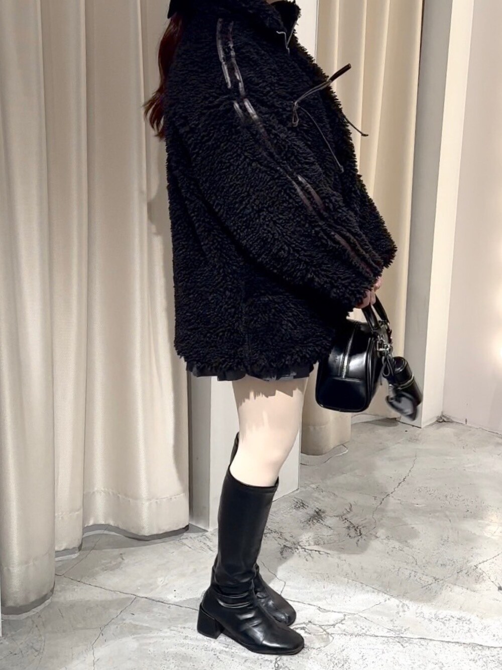 ブラック系のブルゾン、ブラック系のハンドバッグ、グレー系のスカートを着用したレディースの冬コーディネートの2枚目の写真