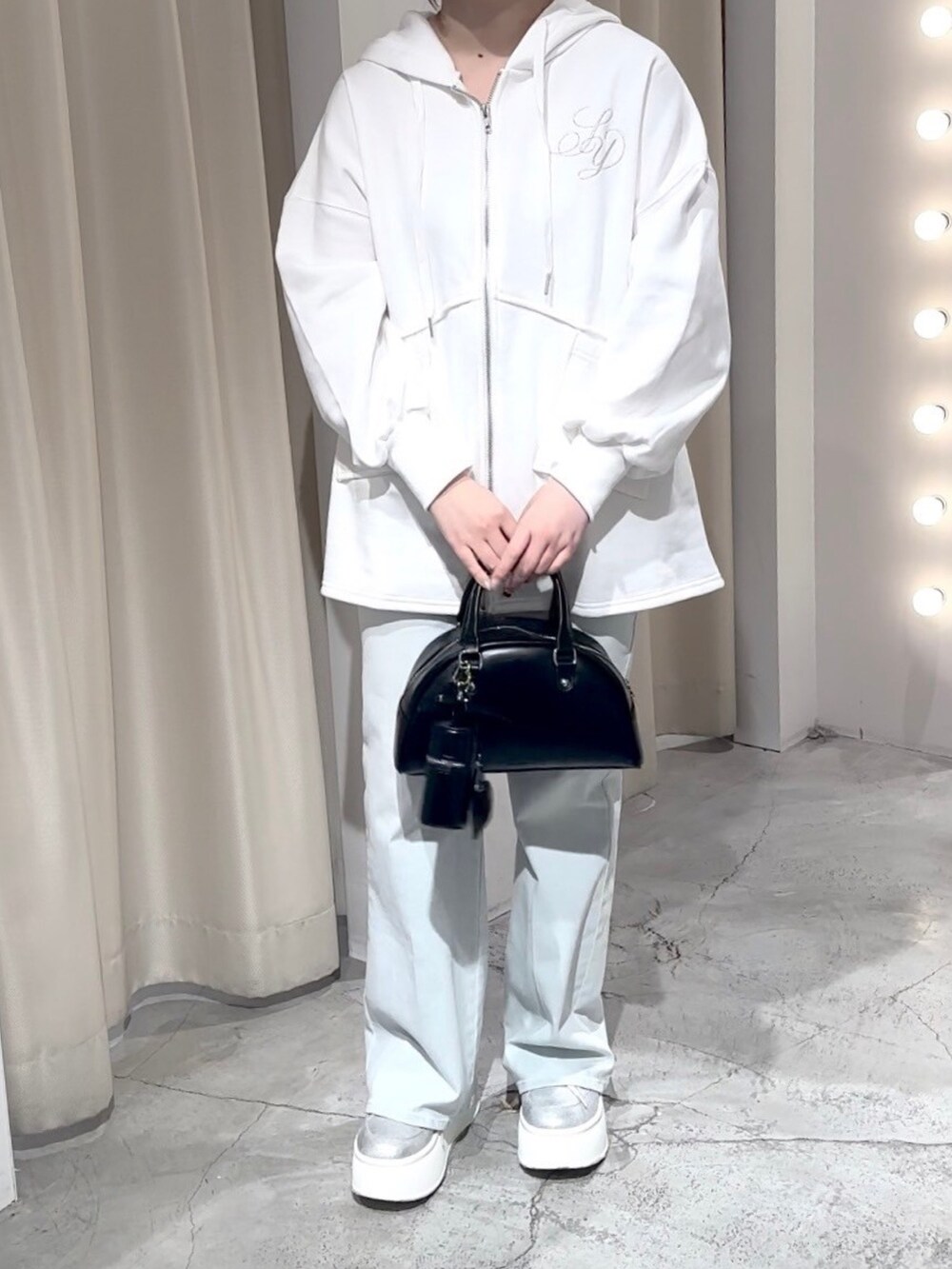 ホワイト系のパーカー、ブラック系のハンドバッグ、ブルー系のデニムパンツを着用したレディースの冬コーディネートの4枚目の写真