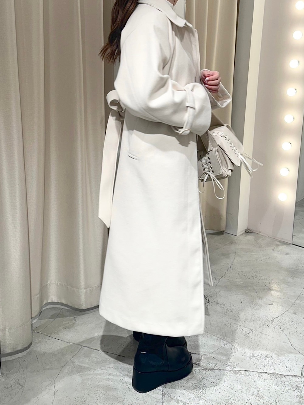ホワイト系のステンカラーコート、ホワイト系のショルダーバッグ、ブラック系のブーツを着用したレディースの冬コーディネートの5枚目の写真