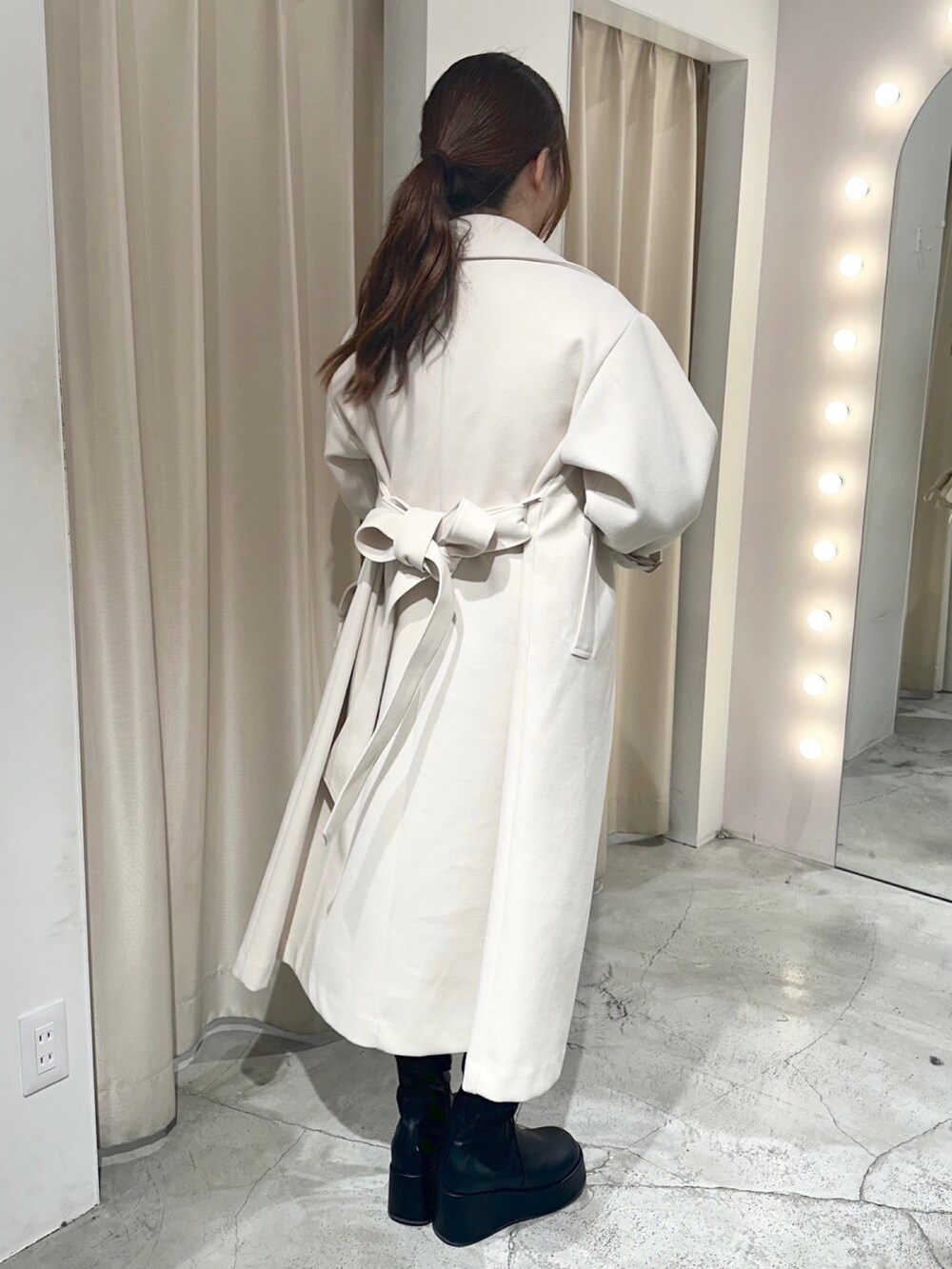 ホワイト系のステンカラーコート、ホワイト系のショルダーバッグ、ブラック系のブーツを着用したレディースの冬コーディネートの6枚目の写真