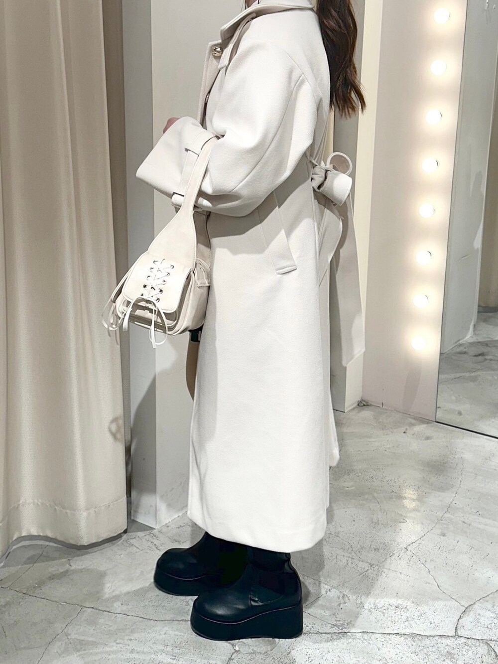 ホワイト系のステンカラーコート、ホワイト系のショルダーバッグ、ブラック系のブーツを着用したレディースの冬コーディネートの3枚目の写真
