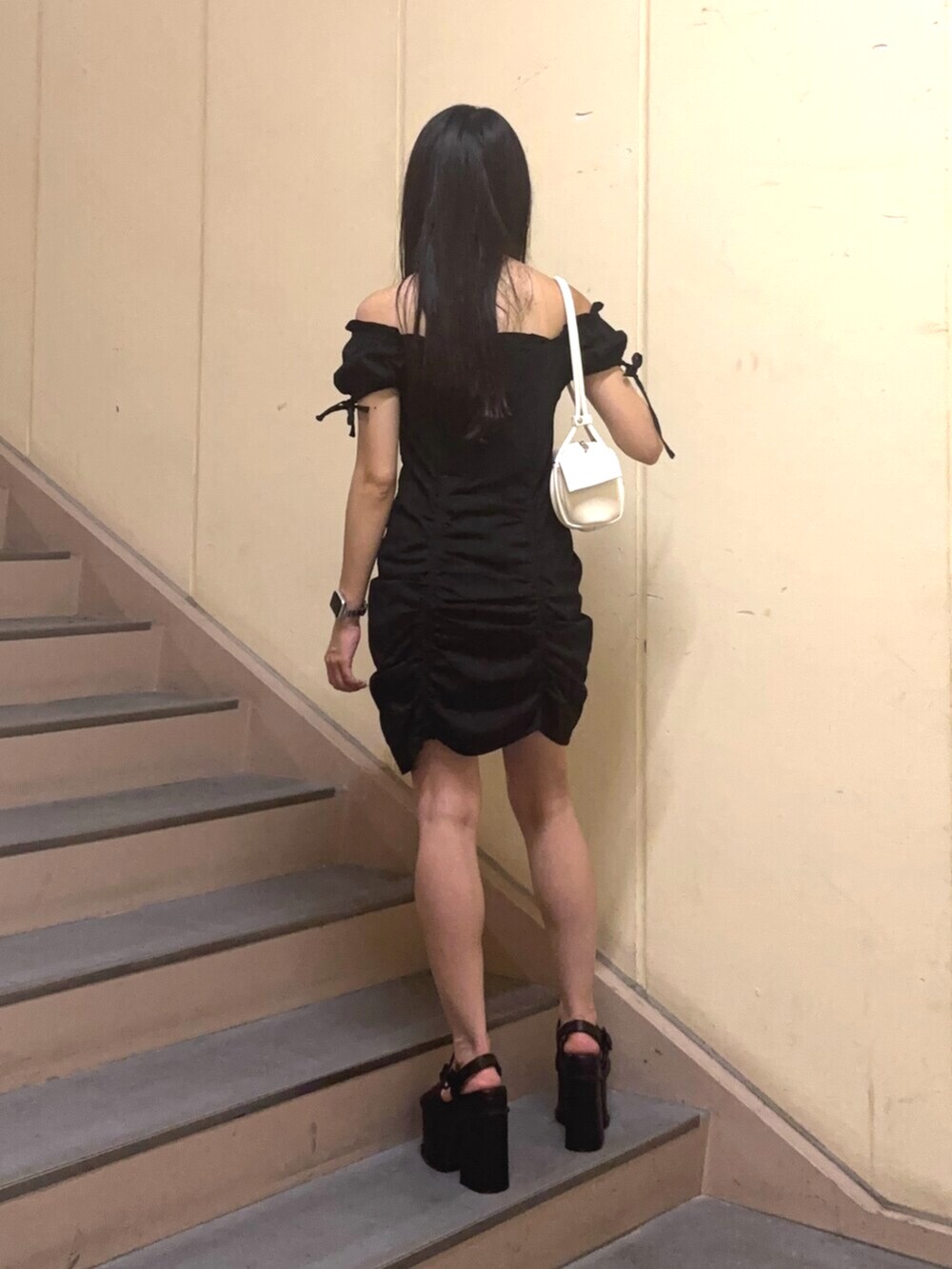 ホワイト系のハンドバッグ、ブラック系のワンピース、ブラック系のサンダルを着用したレディースの夏コーディネートの4枚目の写真