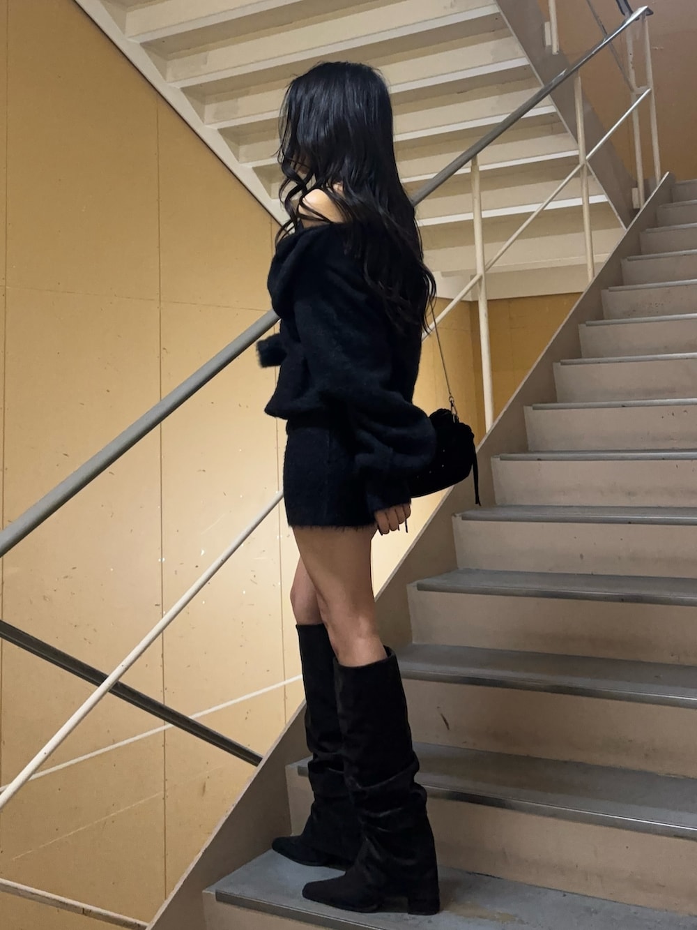 ブラック系のワンピース、ブラック系のブーツ、ブラック系のハンドバッグを着用したレディースの冬コーディネートの3枚目の写真