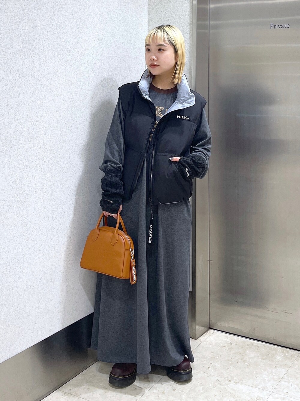 ブラック系のダウンベスト、ブラウン系のボストンバッグ、グレー系のワンピースを着用したレディースの秋コーディネートの2枚目の写真