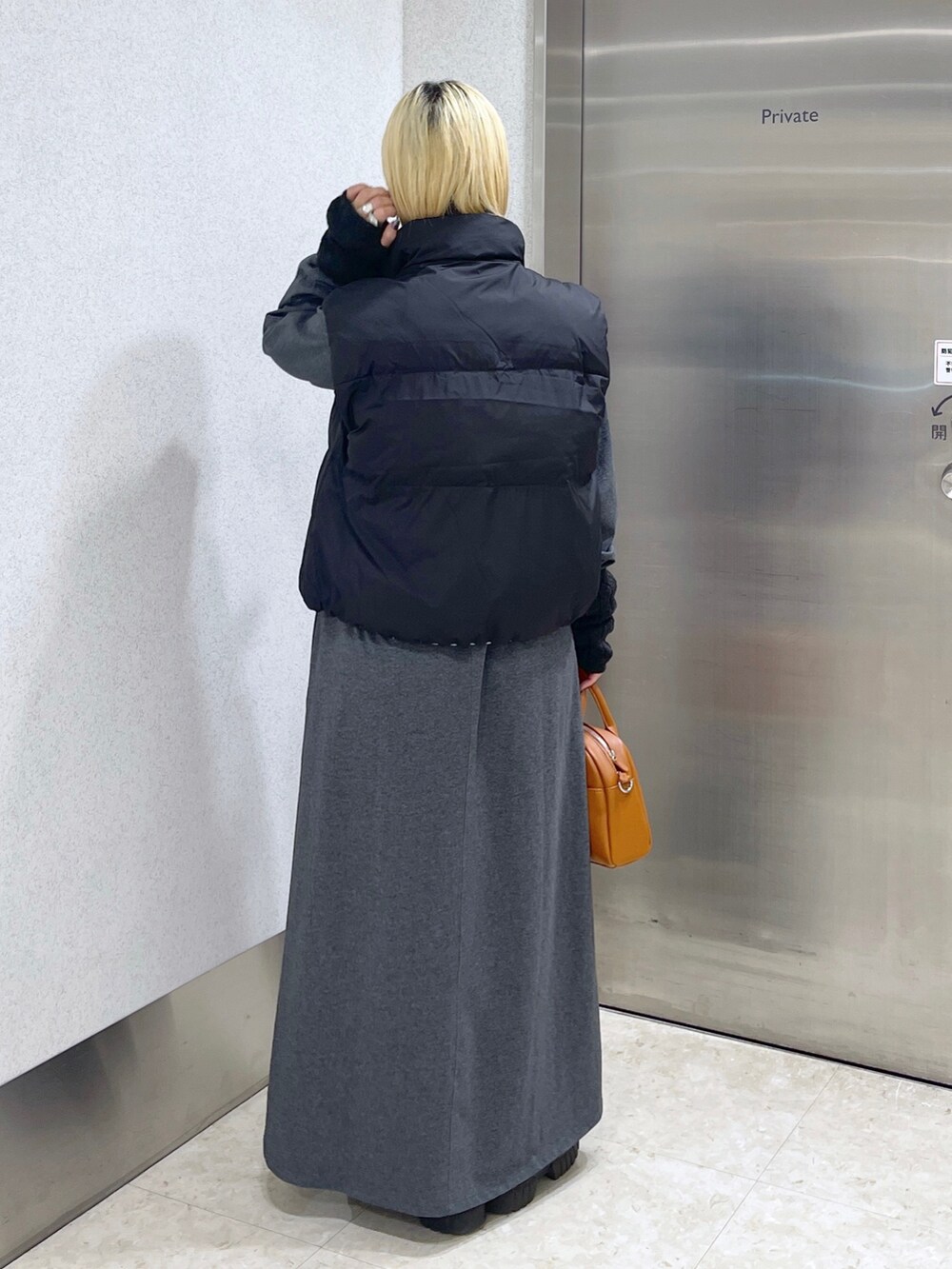 ブラック系のダウンベスト、ブラウン系のボストンバッグ、グレー系のワンピースを着用したレディースの秋コーディネートの4枚目の写真