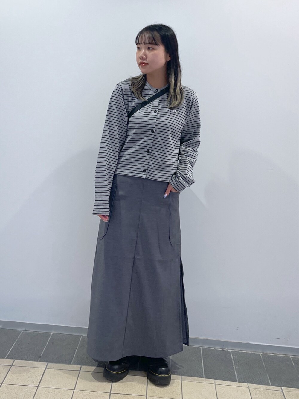 グレー系のスカート、ブラック系のショルダーバッグ、グレー系のカーディガン/ボレロを着用したレディースの秋コーディネートの2枚目の写真