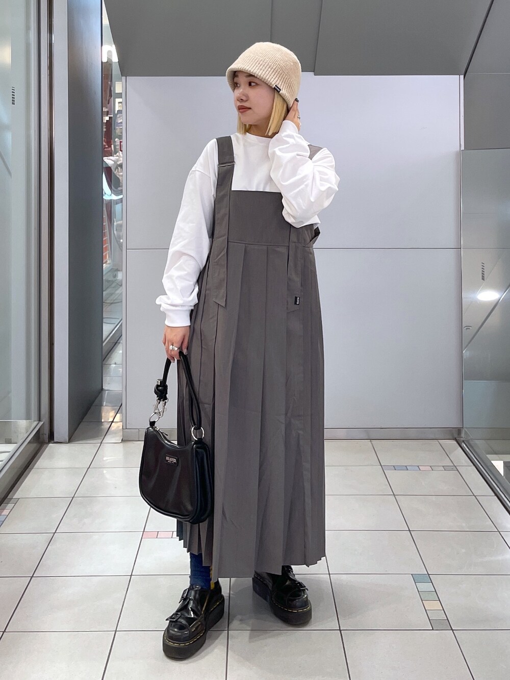 ホワイト系のTシャツ/カットソー、グレー系のジャンパースカート、ブラック系のショルダーバッグを着用したレディースの冬コーディネートの2枚目の写真