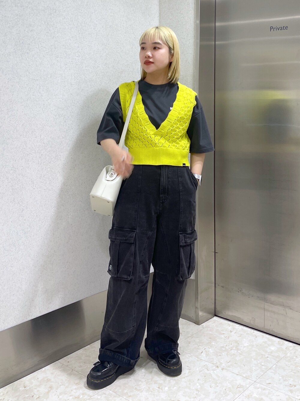 イエロー系のベスト、ホワイト系のショルダーバッグ、ブラック系のカーゴパンツを着用したレディースの春コーディネートの2枚目の写真