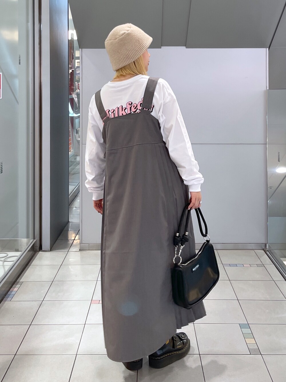 ホワイト系のTシャツ/カットソー、グレー系のジャンパースカート、ブラック系のショルダーバッグを着用したレディースの冬コーディネートの4枚目の写真