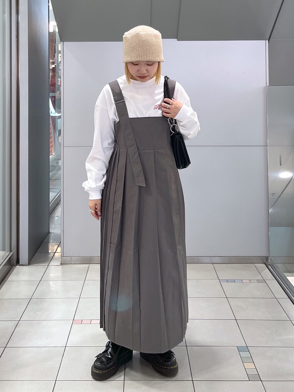 ホワイト系のTシャツ/カットソー、グレー系のジャンパースカート、ブラック系のショルダーバッグを着用したレディースの冬コーディネートの3枚目の写真