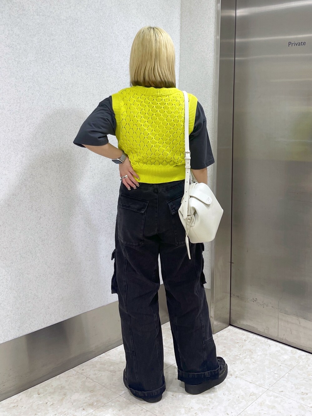 イエロー系のベスト、ホワイト系のショルダーバッグ、ブラック系のカーゴパンツを着用したレディースの春コーディネートの4枚目の写真