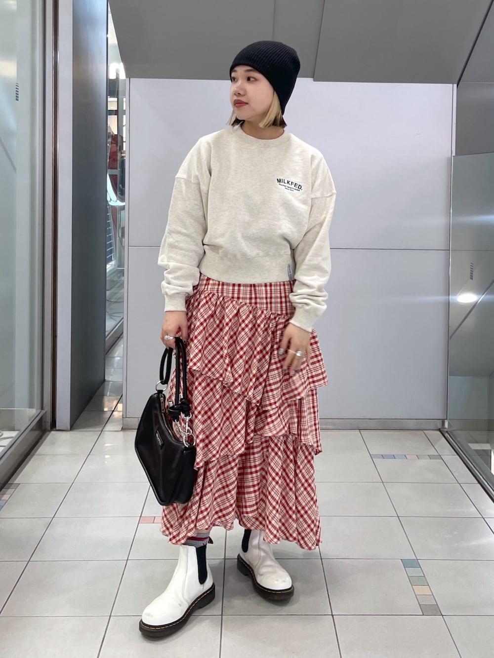 レッド系のスカート、ベージュ系のスウェット、ブラック系のショルダーバッグを着用したレディースの冬コーディネートの2枚目の写真