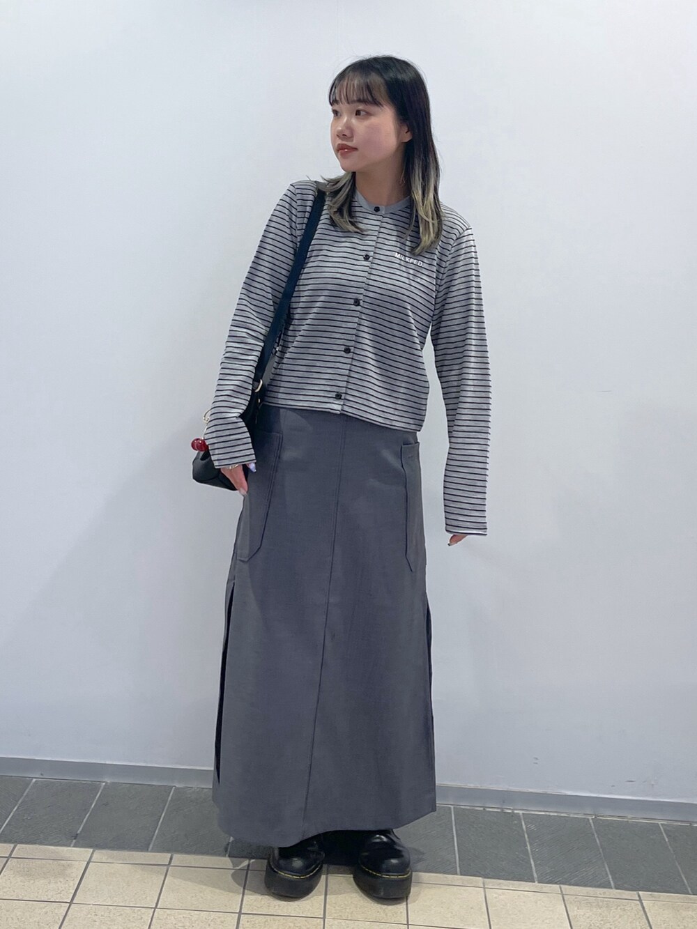 グレー系のスカート、ブラック系のショルダーバッグ、グレー系のカーディガン/ボレロを着用したレディースの秋コーディネートの3枚目の写真