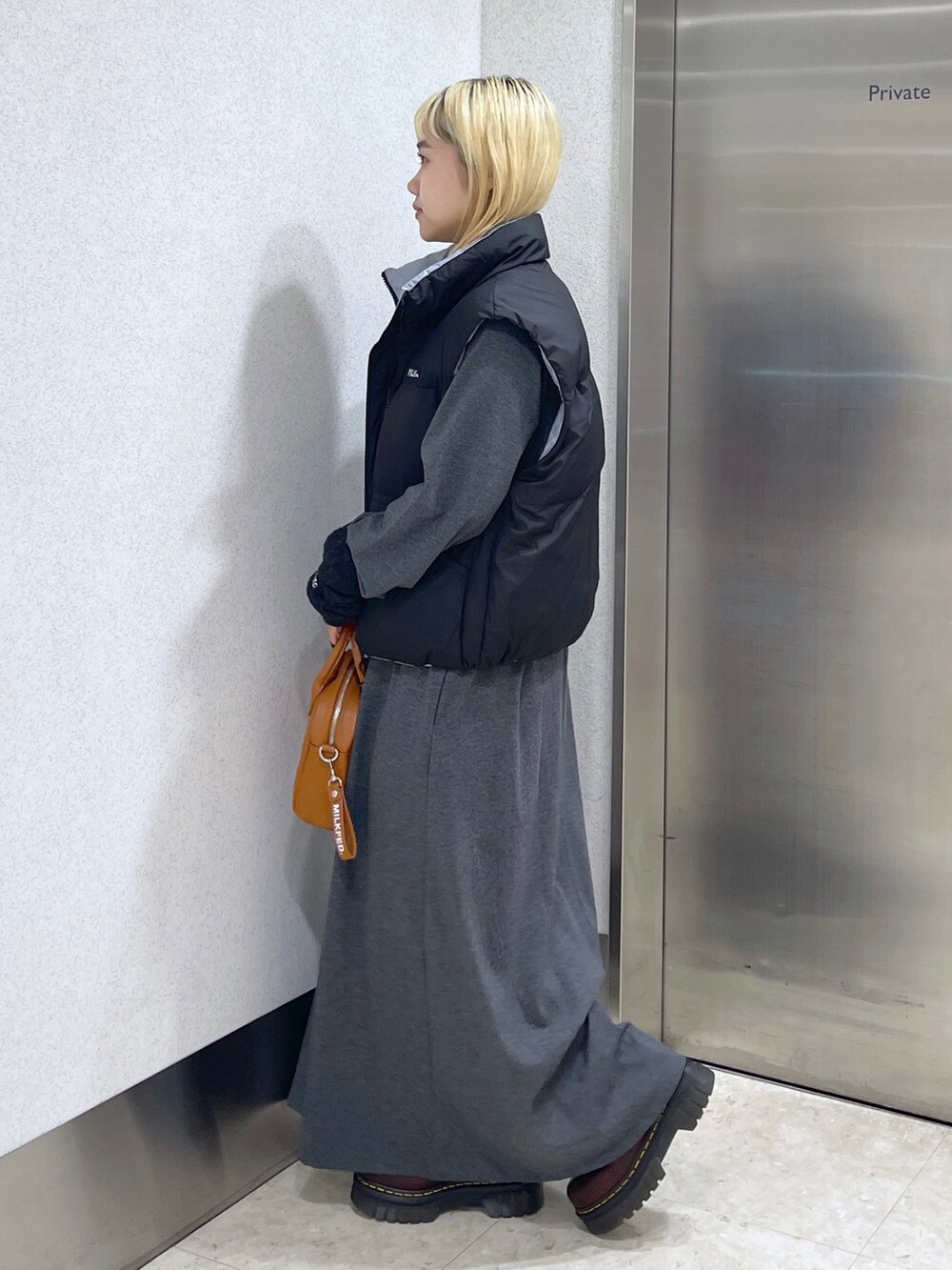 ブラック系のダウンベスト、ブラウン系のボストンバッグ、グレー系のワンピースを着用したレディースの秋コーディネートの3枚目の写真