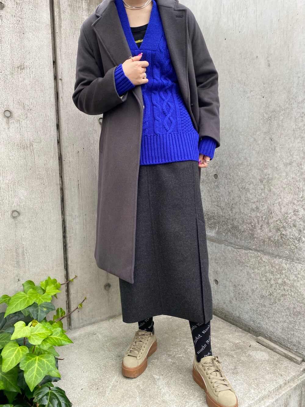 グレー系のチェスターコート、グレー系のスカート、ブルー系のニット/セーターを着用したレディースの冬コーディネートの2枚目の写真