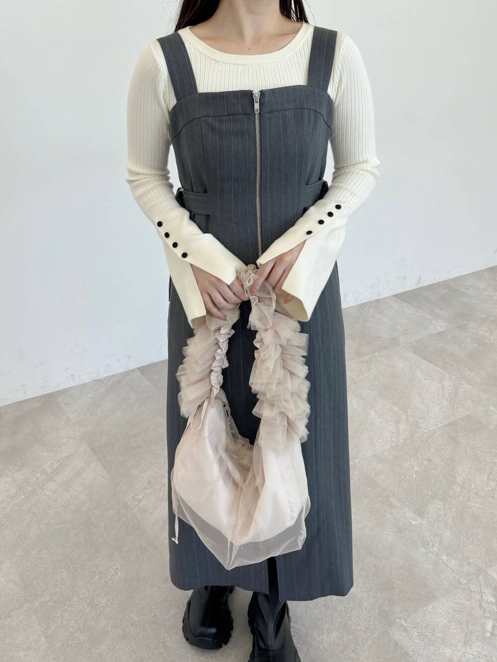 ブラック系のブーツ、ベージュ系のショルダーバッグ、グレー系のジャンパースカートを着用したレディースの冬コーディネートの3枚目の写真