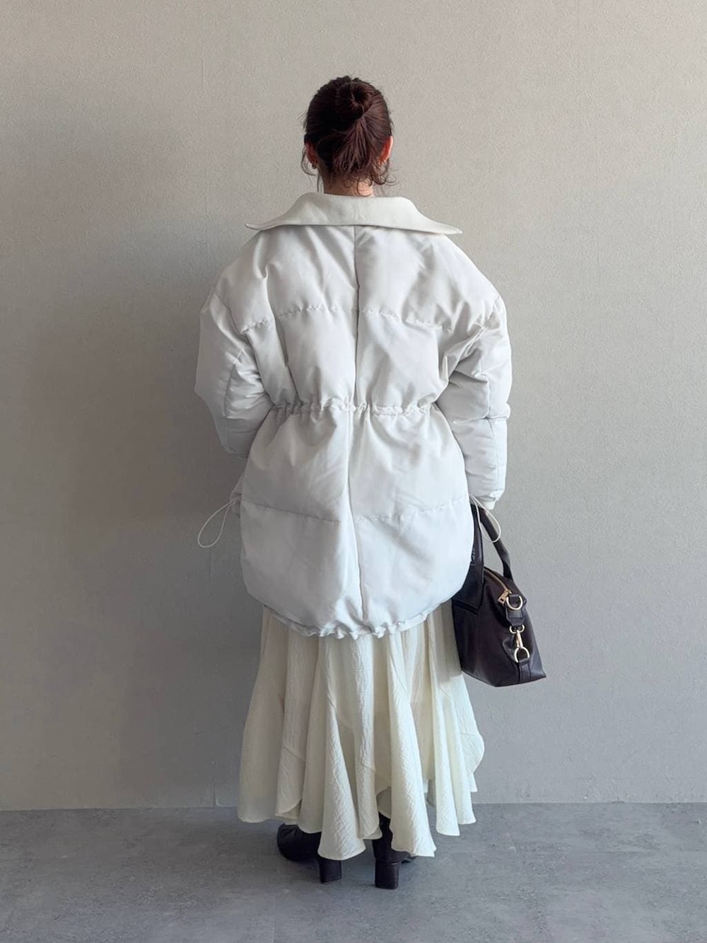 ブラウン系のボストンバッグ、ホワイト系のスカート、ブラウン系のブーツを着用したレディースの冬コーディネートの2枚目の写真