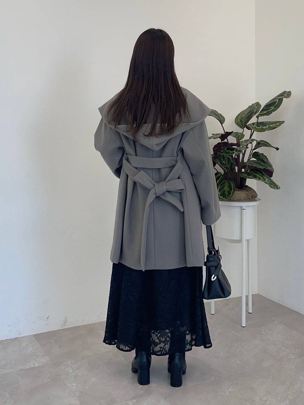 グレー系のノーカラーコート、ブラック系のショルダーバッグ、ブラック系のブーツを着用したレディースの冬コーディネートの2枚目の写真