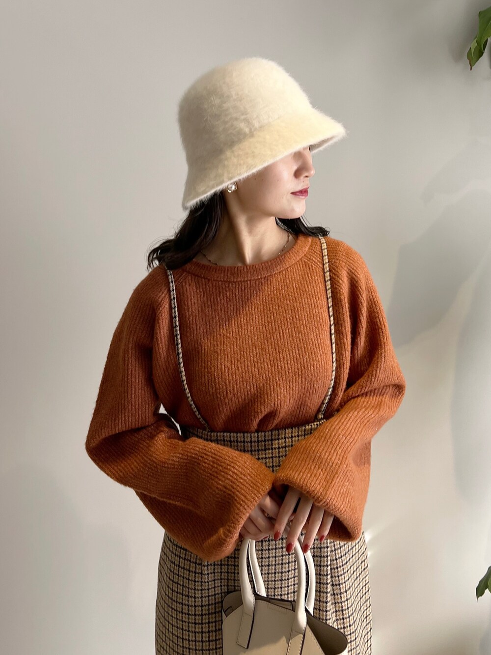 オレンジ系のニット/セーター、ベージュ系のスカート、ホワイト系のショルダーバッグを着用したレディースの冬コーディネートの3枚目の写真