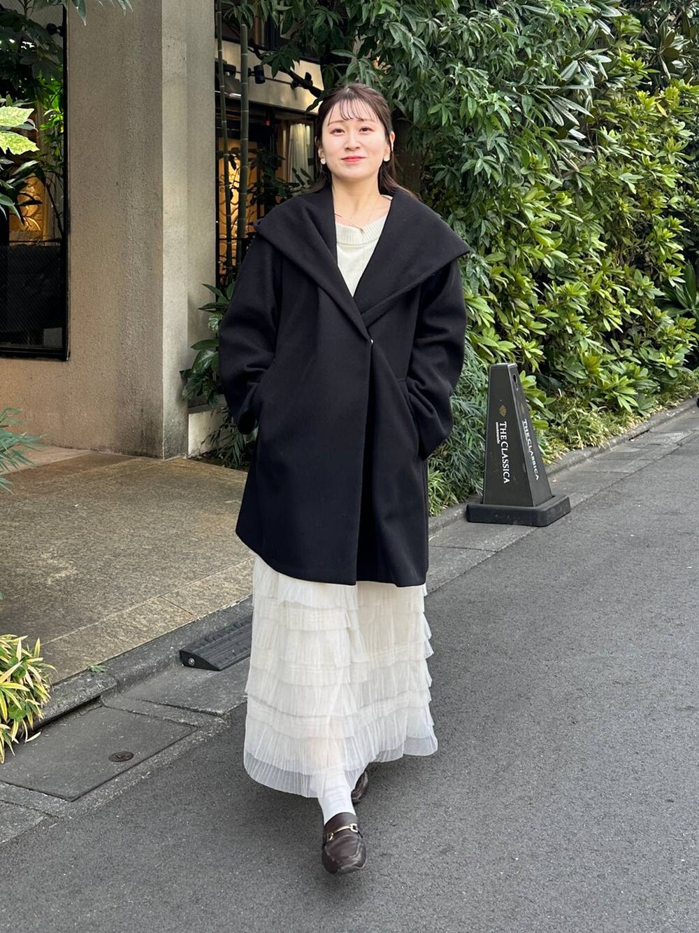 ブラック系のノーカラーコート、ホワイト系のスカートを着用したレディースの冬コーディネートの2枚目の写真