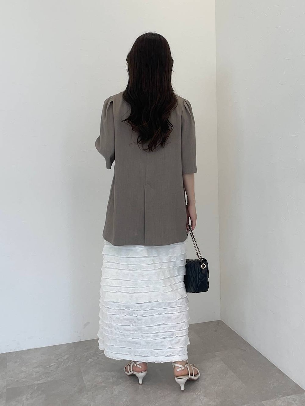 ベージュ系のテーラードジャケット、ホワイト系のワンピース、ブラック系のショルダーバッグを着用したレディースの夏コーディネートの2枚目の写真