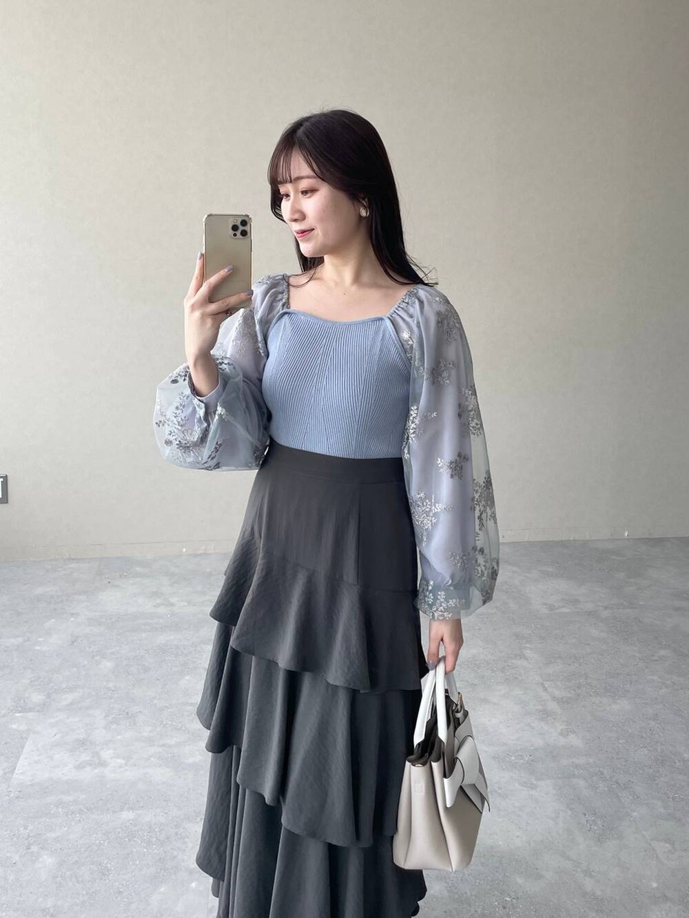 グレー系のスカート、ベージュ系のショルダーバッグ、ブルー系のニット/セーターを着用したレディースの春コーディネートの3枚目の写真