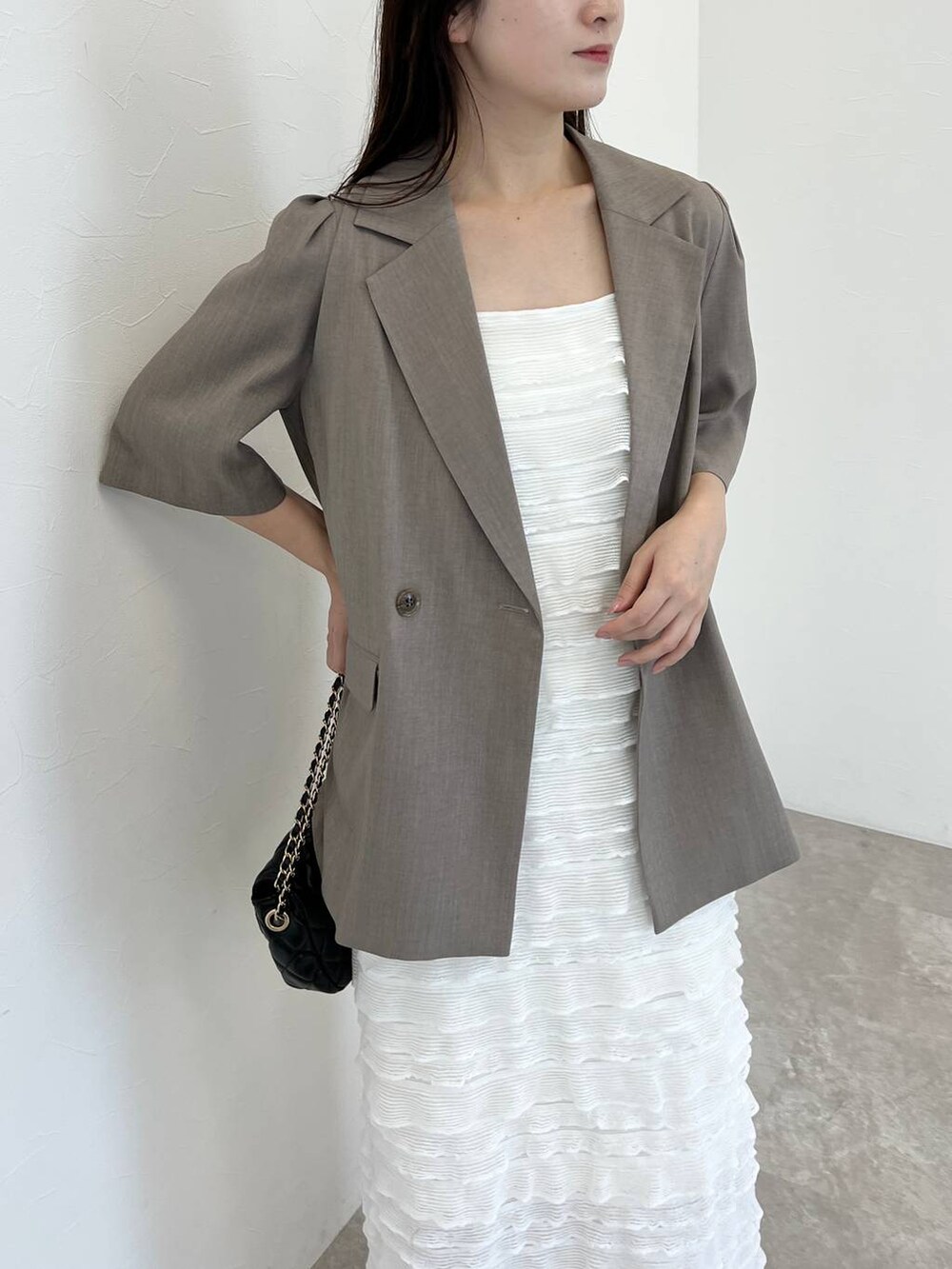 ベージュ系のテーラードジャケット、ホワイト系のワンピース、ブラック系のショルダーバッグを着用したレディースの夏コーディネートの3枚目の写真