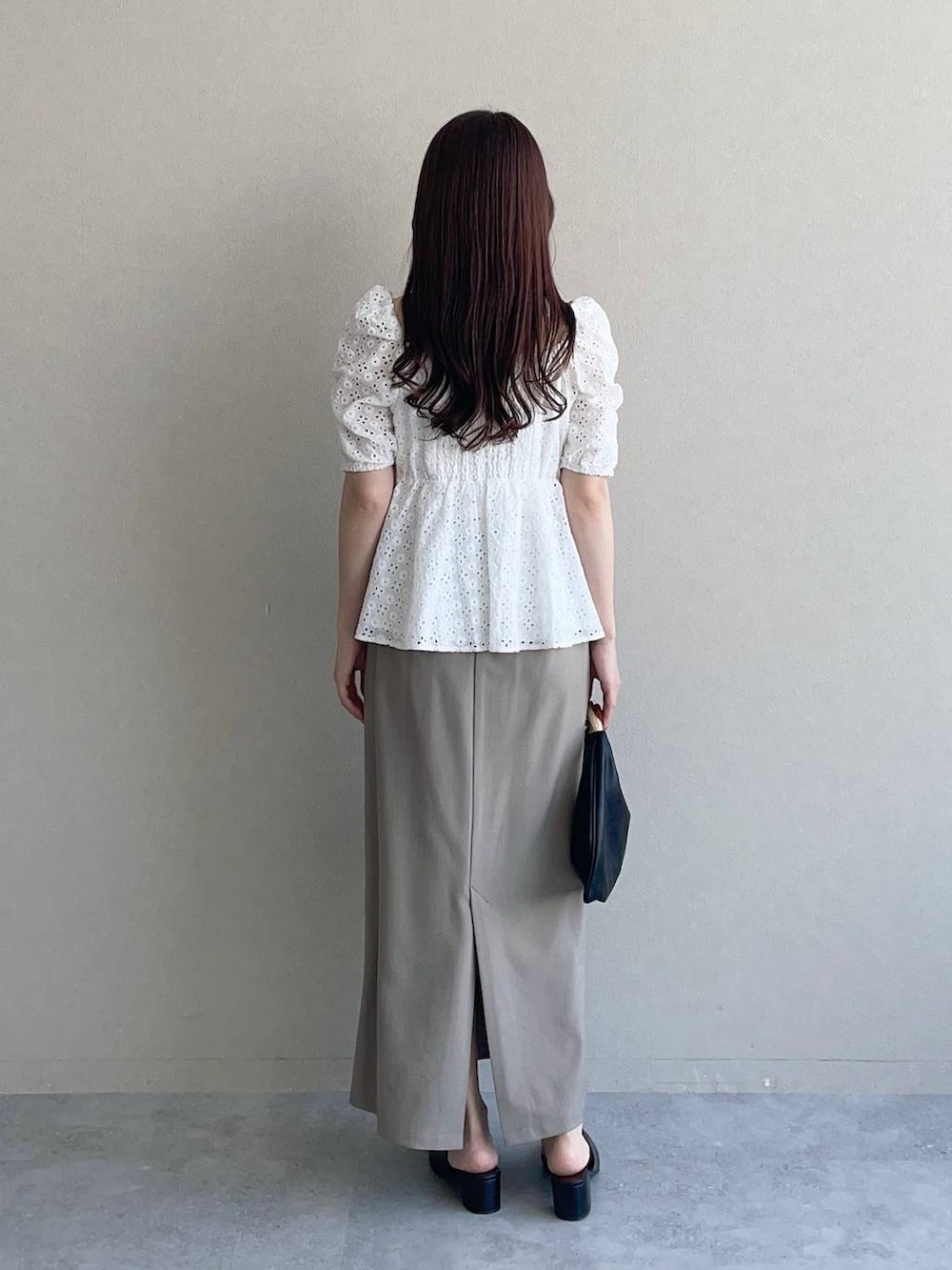 ブラック系のハンドバッグ、ベージュ系のスカート、ホワイト系のシャツ/ブラウスを着用したレディースの夏コーディネートの2枚目の写真