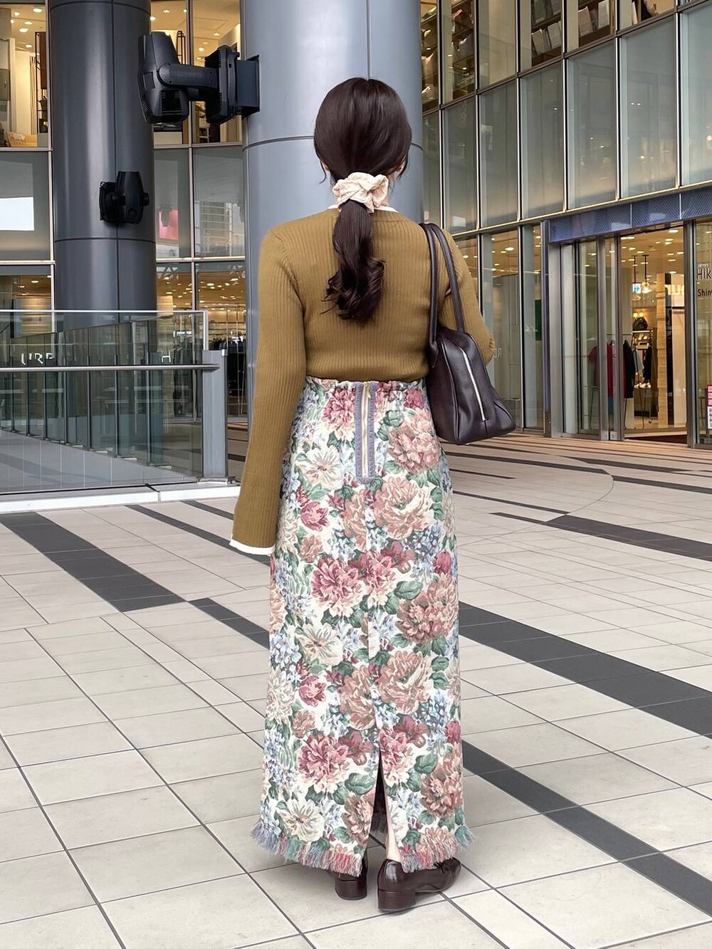 ブルー系のスカート、ブラウン系のトートバッグ、グリーン系のニット/セーターを着用したレディースの秋コーディネートの2枚目の写真