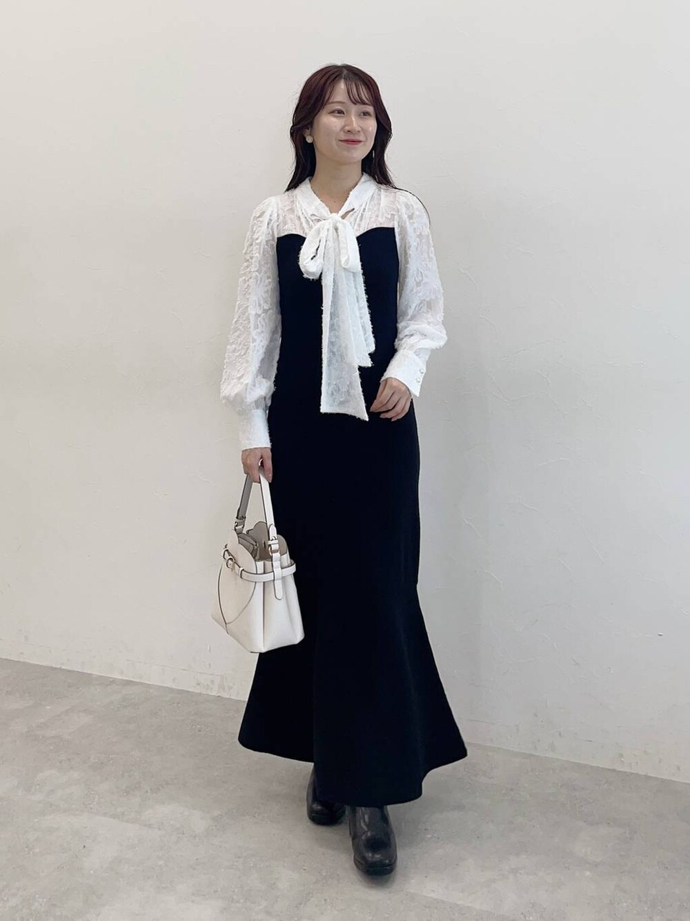 ブラック系のチェスターコート、ブラック系のワンピース、ホワイト系のショルダーバッグを着用したレディースの秋コーディネートの5枚目の写真