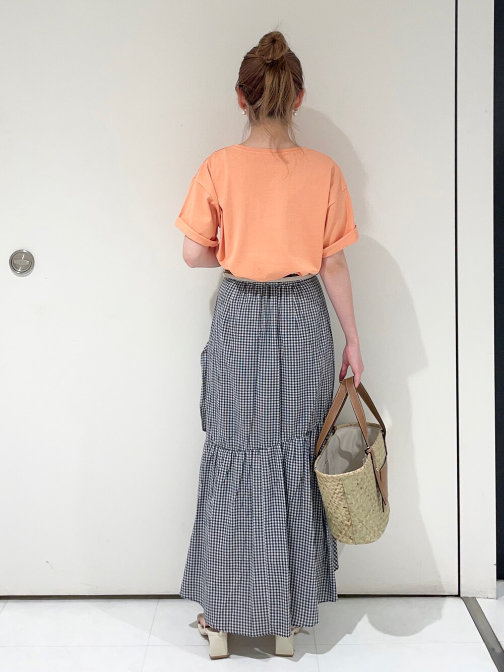 オレンジ系のTシャツ/カットソー、ブラック系のスカート、ベージュ系のハンドバッグを着用したレディースの夏コーディネートの2枚目の写真