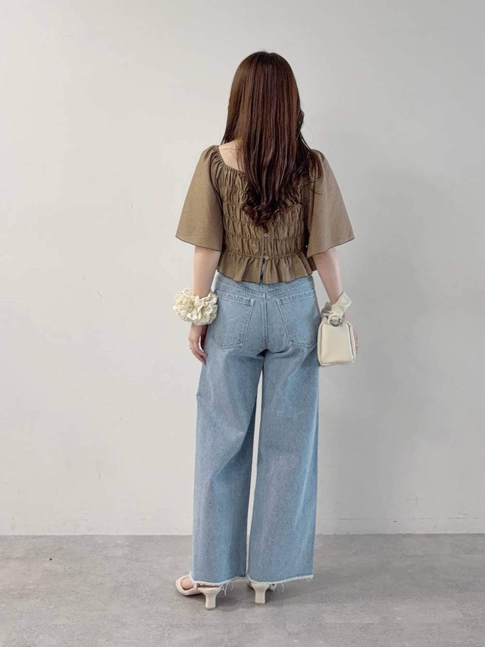 ブラウン系のワンピース、ブルー系のデニムパンツ、ホワイト系のサンダルを着用したレディースの秋コーディネートの2枚目の写真