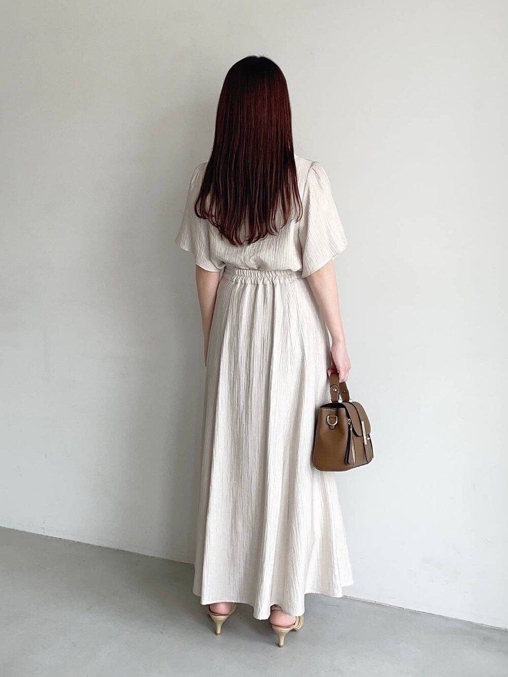 ゴールド系のパンプス、ブラウン系のショルダーバッグ、ベージュ系のスカートを着用したレディースの夏コーディネートの2枚目の写真