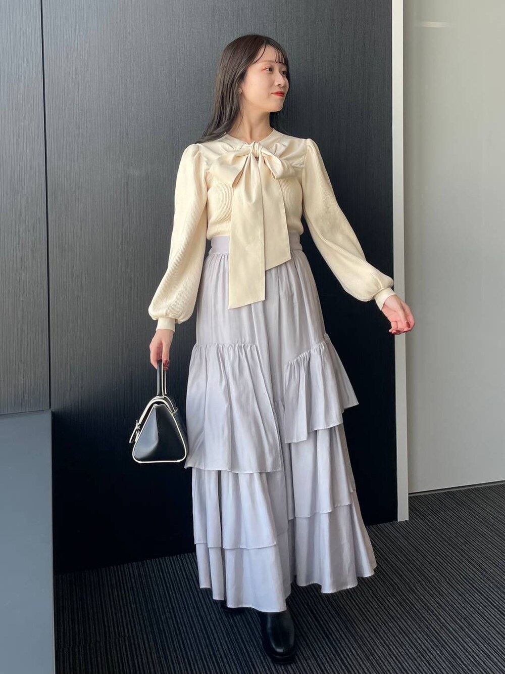 グレー系のチェスターコート、ブラック系のハンドバッグ、ブラック系のブーツを着用したレディースの秋コーディネートの3枚目の写真