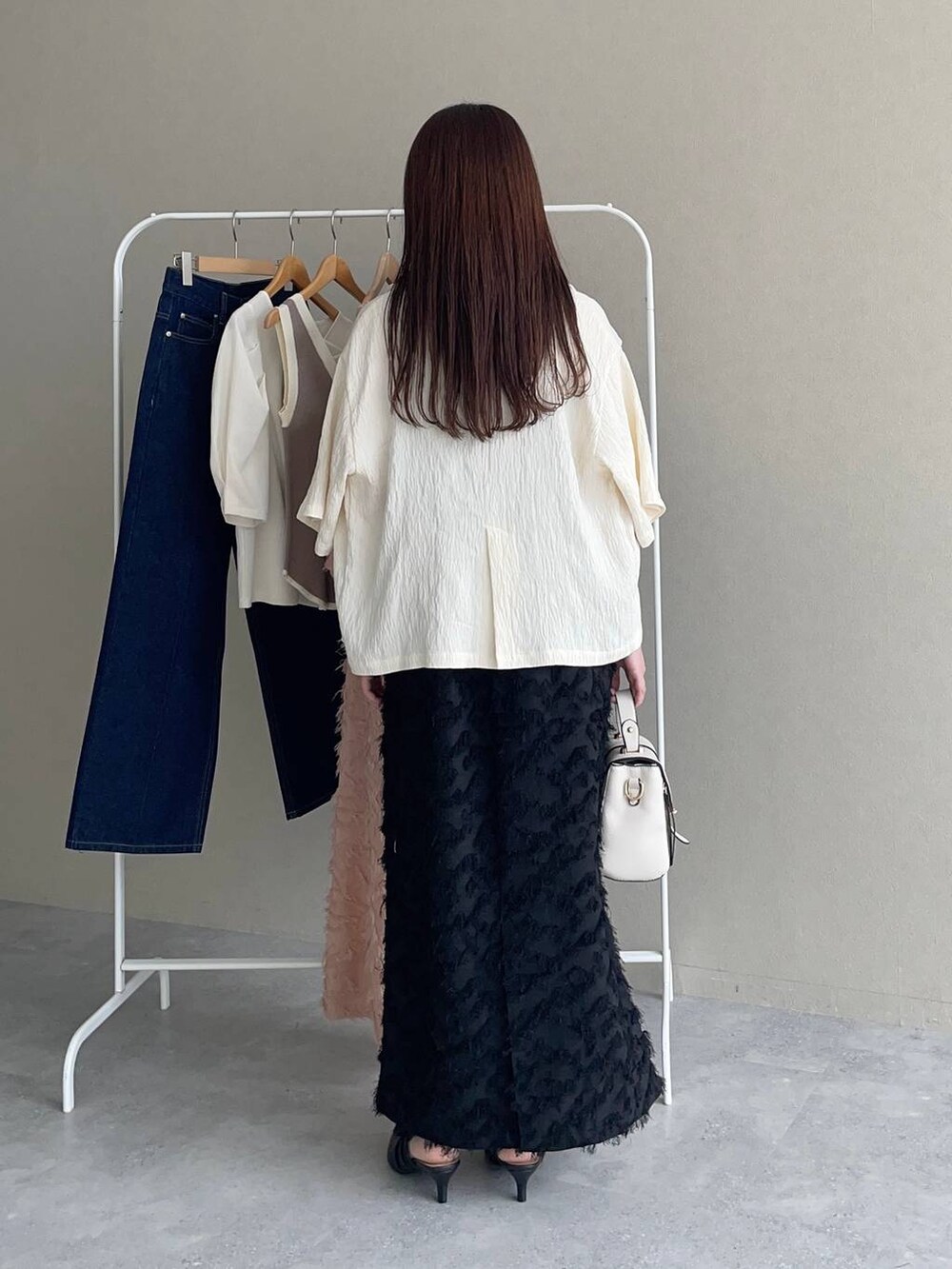 ホワイト系のテーラードジャケット、ブラック系のパンプス、ホワイト系のショルダーバッグを着用したレディースの夏コーディネートの2枚目の写真