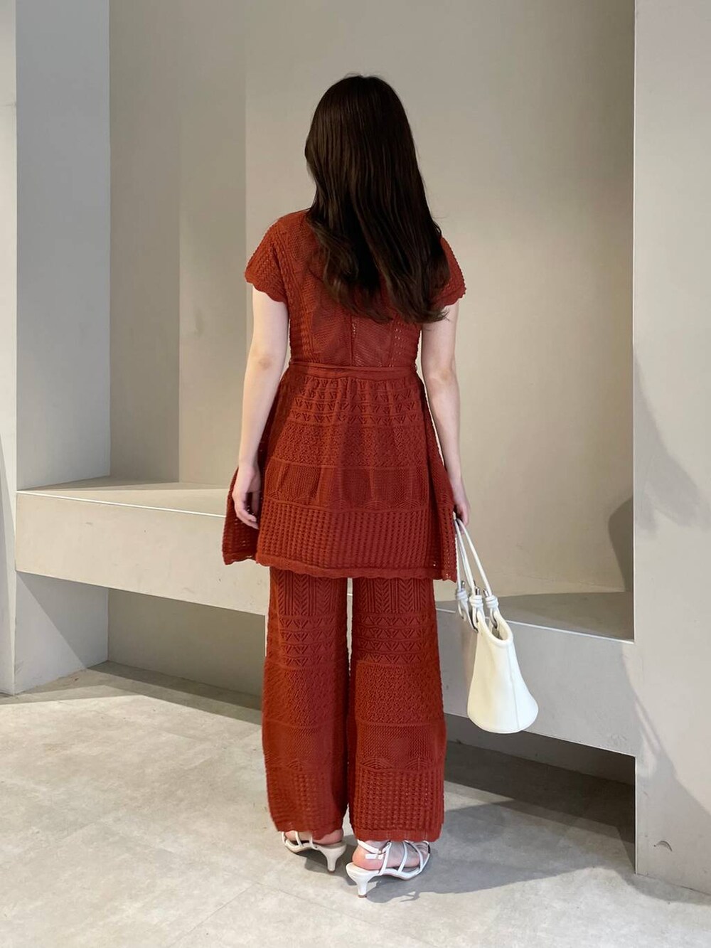 ホワイト系のハンドバッグ、オレンジ系のニット/セーター、ホワイト系のサンダルを着用したレディースの春コーディネートの2枚目の写真