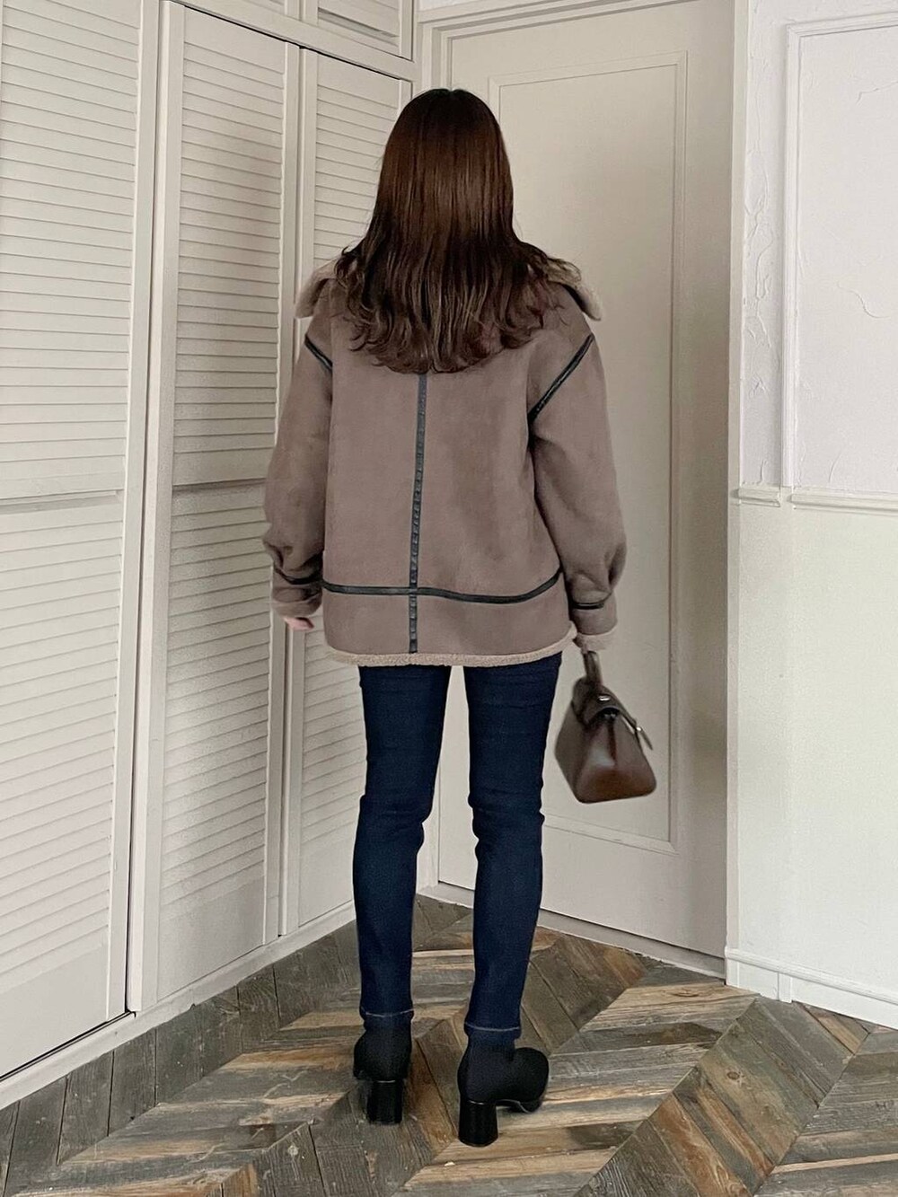 ブルー系のデニムパンツ、ブラウン系のハンドバッグ、ブラック系のブーツを着用したレディースの秋コーディネートの2枚目の写真