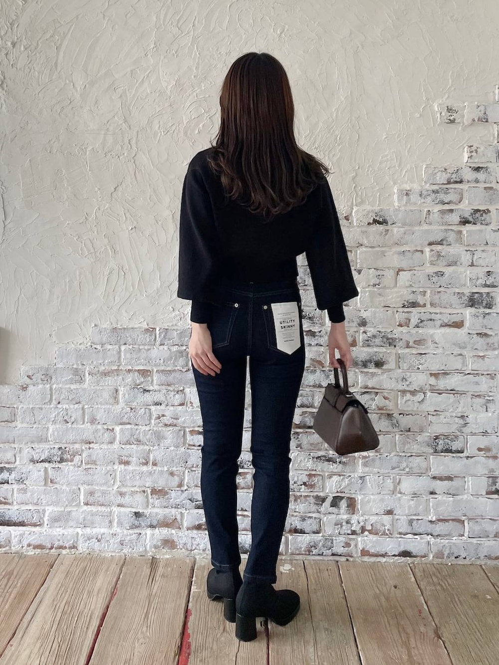 ブルー系のデニムパンツ、ブラウン系のハンドバッグ、ブラック系のブーツを着用したレディースの冬コーディネートの2枚目の写真