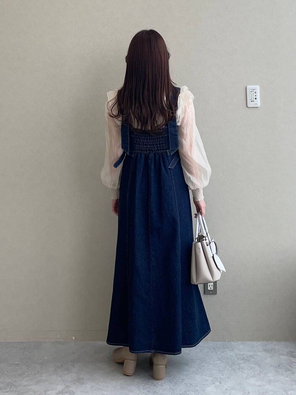 ブルー系のジャンパースカート、ベージュ系のショルダーバッグ、ブラウン系のパンプスを着用したレディースの冬コーディネートの2枚目の写真