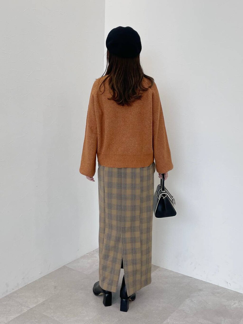 オレンジ系のニット/セーター、ブラック系のハンドバッグ、ブラック系のブーツを着用したレディースの秋コーディネートの2枚目の写真