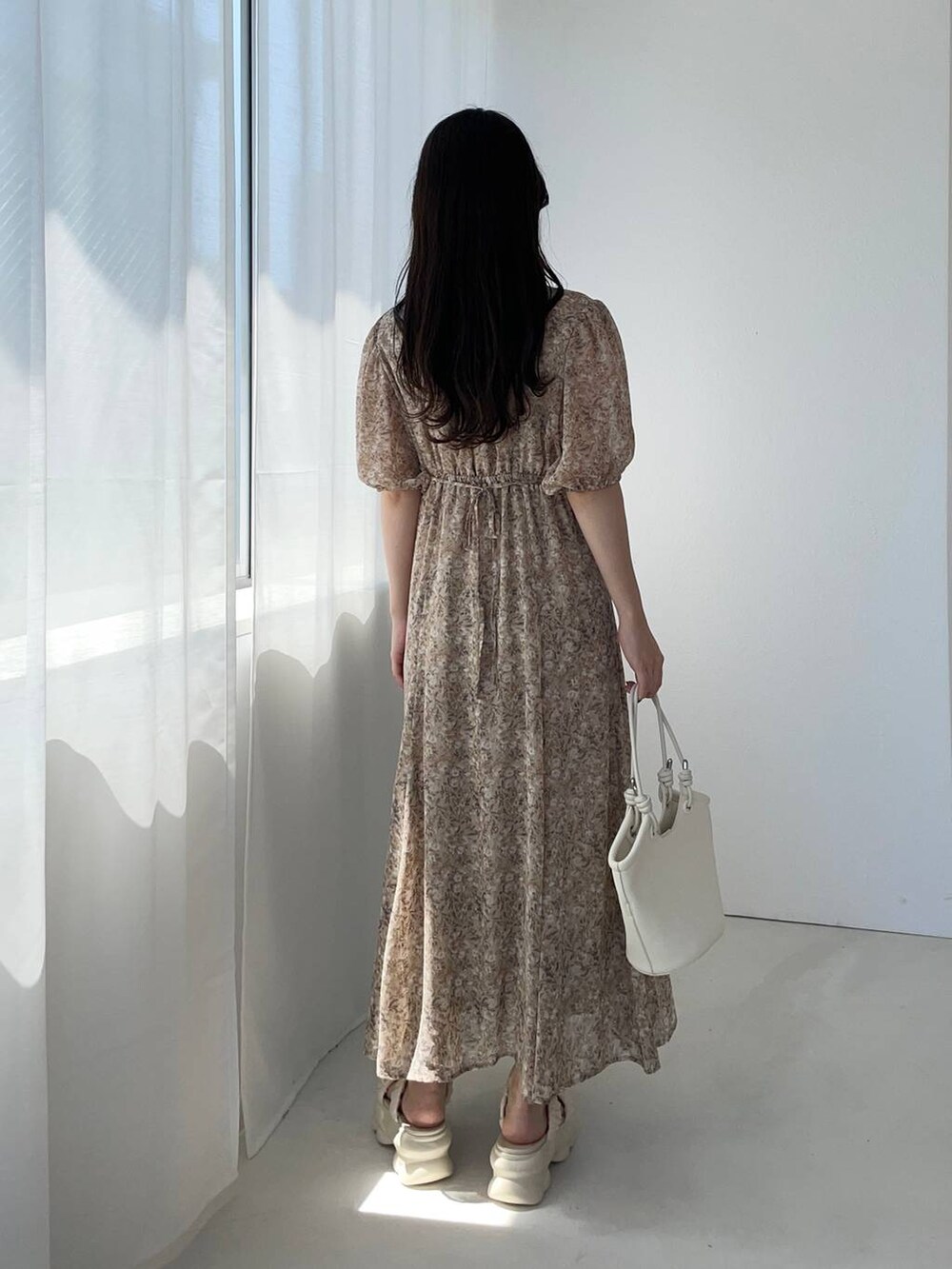 ホワイト系のハンドバッグ、ホワイト系のサンダル、ベージュ系のワンピースを着用したレディースの夏コーディネートの2枚目の写真