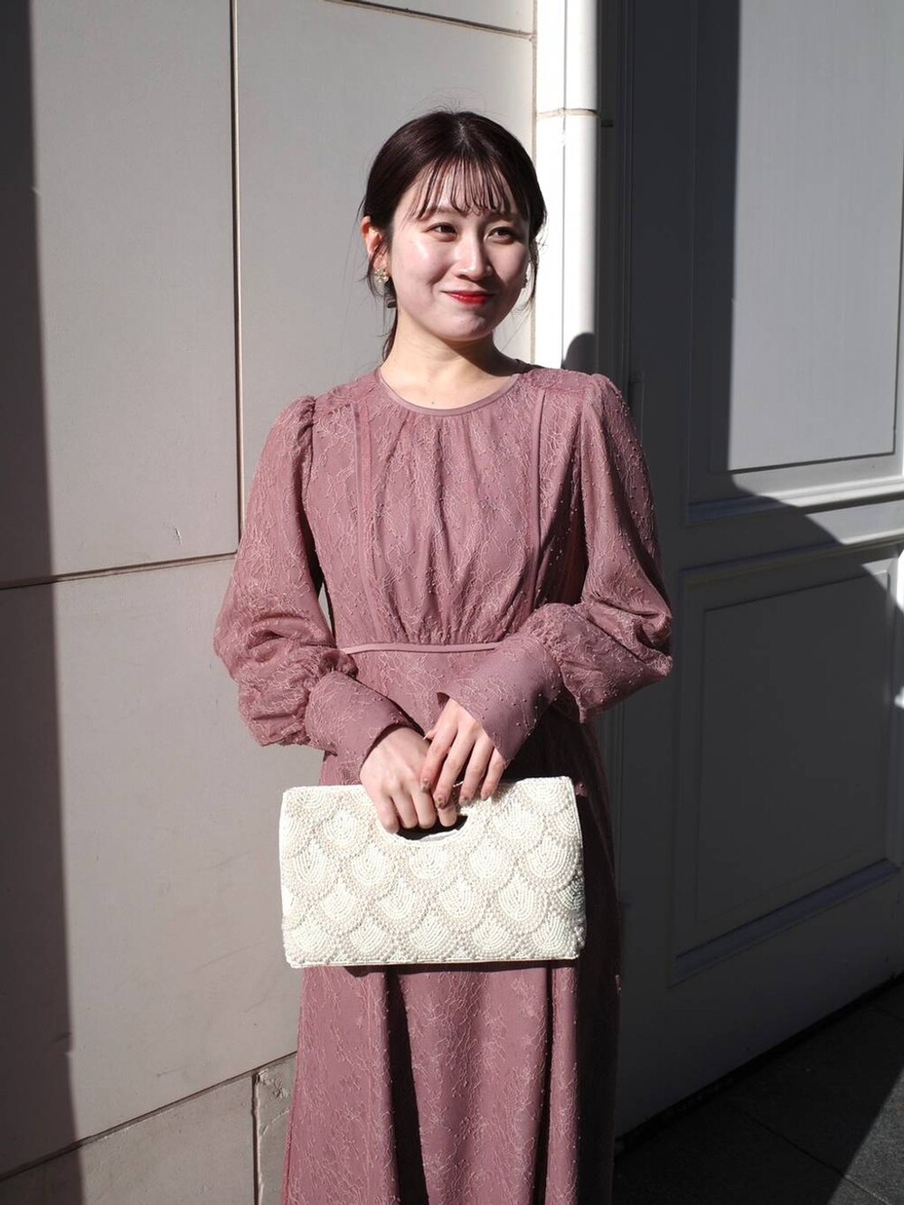 ピンク系のドレス、ベージュ系のクラッチバッグを着用したレディースの冬コーディネートの3枚目の写真