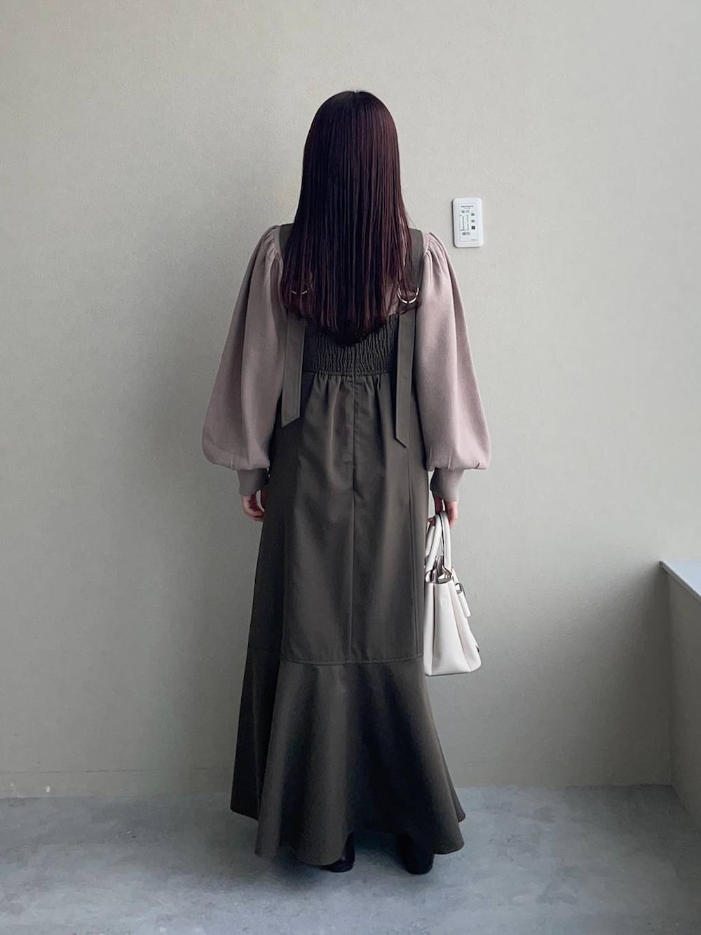 ブラウン系のニット/セーター、ホワイト系のショルダーバッグ、ブラウン系のジャンパースカートを着用したレディースの冬コーディネートの2枚目の写真