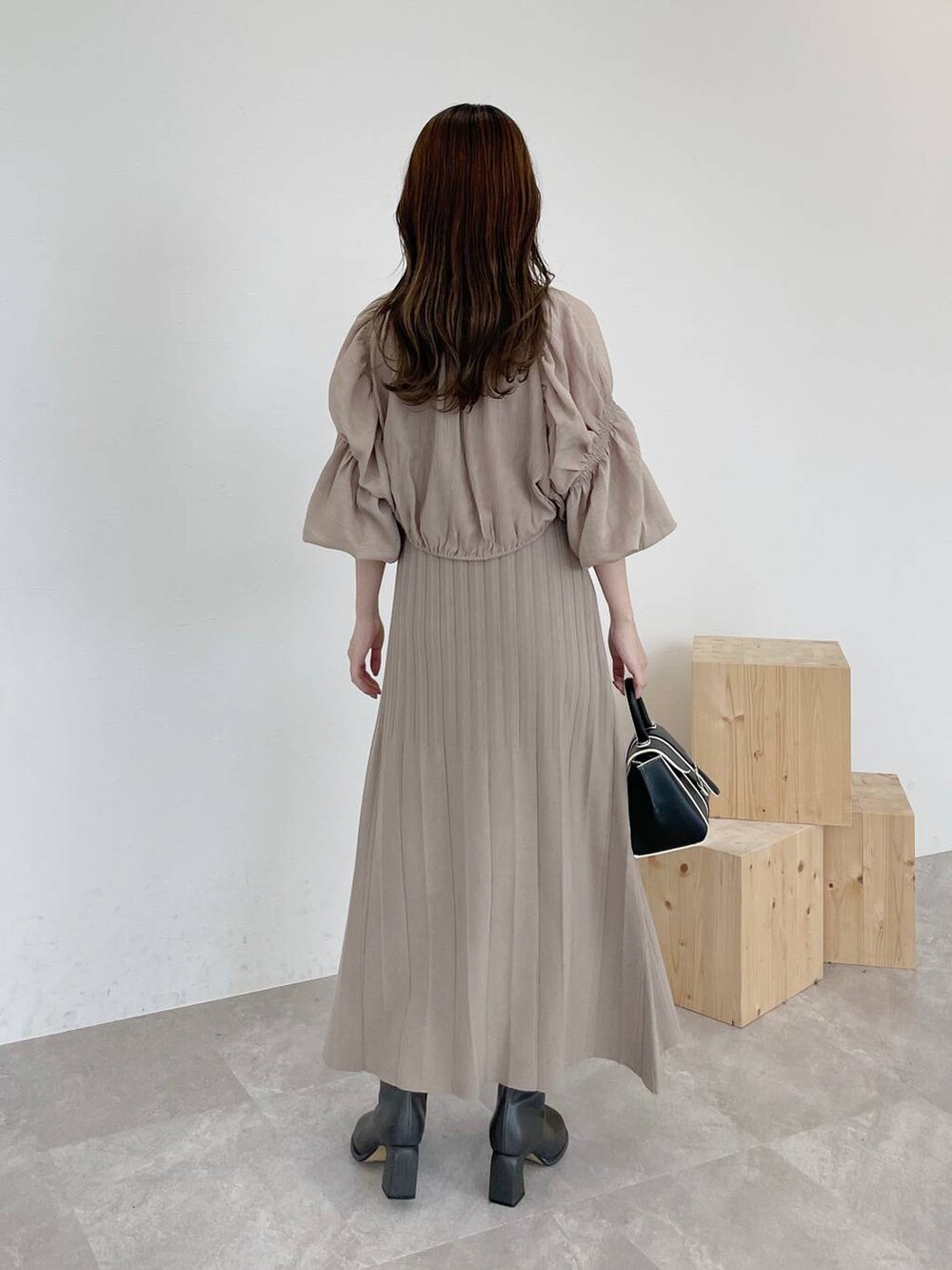 ブラック系のハンドバッグ、グレー系のブーツ、ベージュ系のワンピースを着用したレディースの秋コーディネートの2枚目の写真