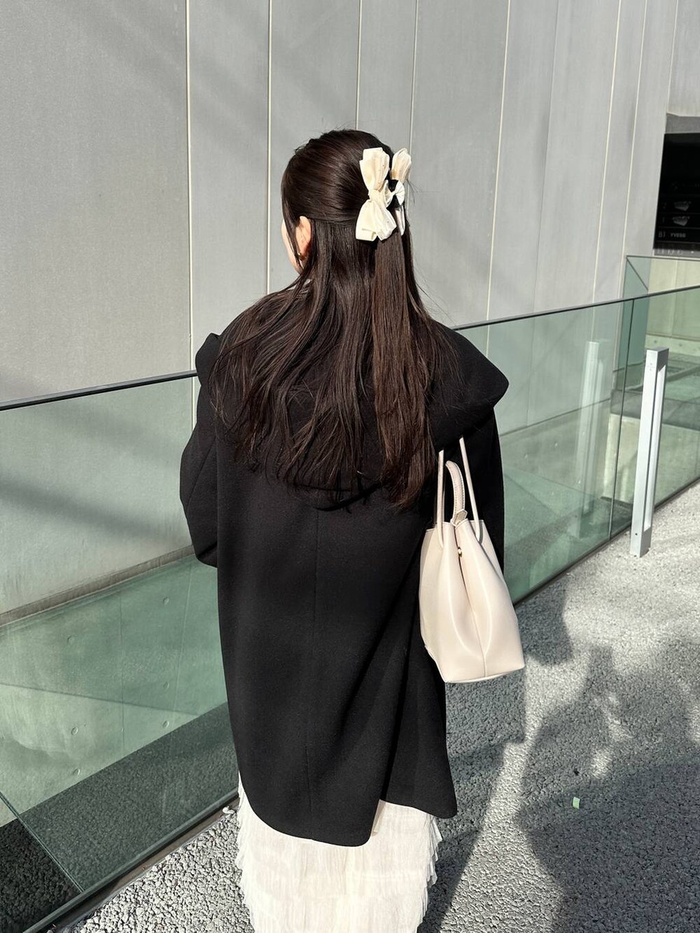 ブラック系のノーカラーコート、ホワイト系のスカートを着用したレディースの冬コーディネートの3枚目の写真