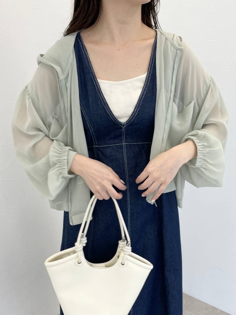 ホワイト系のハンドバッグ、グリーン系のパーカー、ブルー系のジャンパースカートを着用したレディースの春コーディネートの3枚目の写真